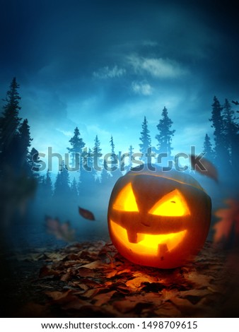 A halloween background with a glowing spooky Jack O Lantern pumpkin outside at night with a forest in the background. Photo composite.