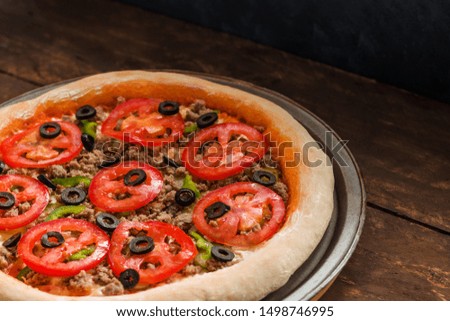 fresh  whole pizza with tomatoes olives pepper meat on tray on wooden table