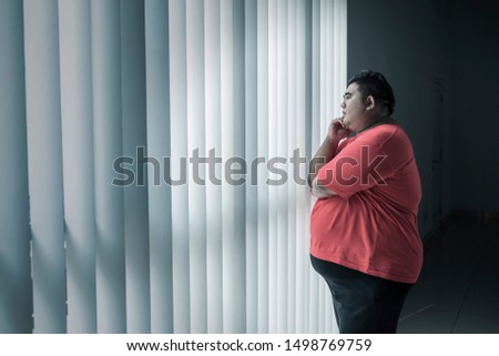 Picture of young fat man thinking something while looking out the window