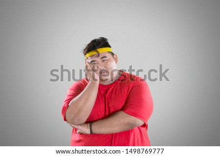 Picture of unhappy fat man thinking something while standing in the studio with gray background