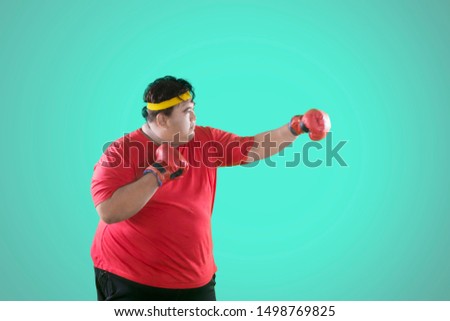 Picture of an overweight man wearing red boxing gloves while punching copy space in the studio