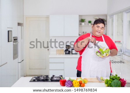 Picture of overweight man mixing fresh vegetables in a bowl while standing in the kitchen