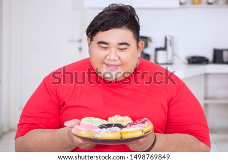 Picture of overweight man looks happy while holding a tasty donuts in the kitchen