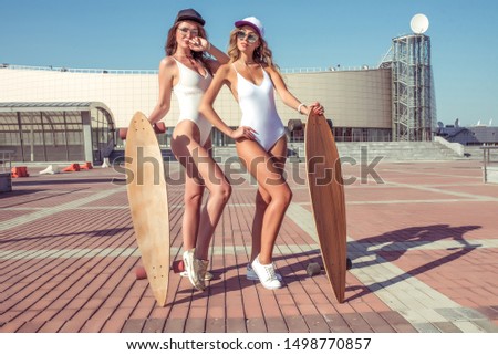 Two girlfriends in summer in city, fashion style youth swimsuits with longboards, rest, sunbathe, concept fashion style youth, lifestyle fitness workout, posing best friends sisters.