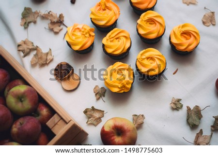 Autumn yellow and orange cupcakes on a light background with autumn dead leaves, pumpkins and apples. Autumn sweets with cream for children. Carrot cupcakes on autumn background