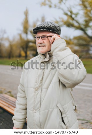 An old man in a jacket and a cap holds glasses in his hand and looks into the distance. Hyperopia, myopia. The concept of retirement age and poor eyesight. Royalty-Free Stock Photo #1498776740