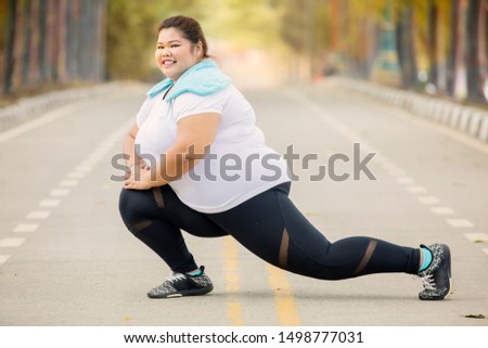 Picture of fat woman smiling at the camera while stretching legs on the road at autumn time