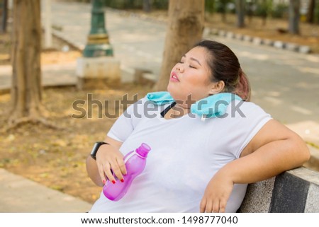 Picture of fat woman holding a bottle of water while resting in the park after exercise