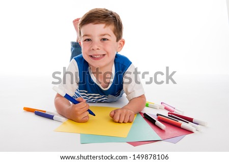 Smiling young boy with felt pens writing and drawing on  colorful paper. White background.