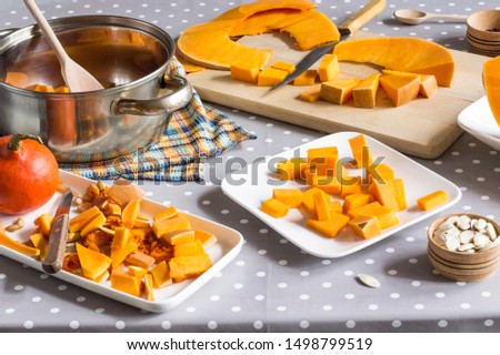Preparation of products for making pumpkin soup. On the table are pumpkin, seeds. Sliced pumpkin on a cutting board. Gray polka dot tablecloth
