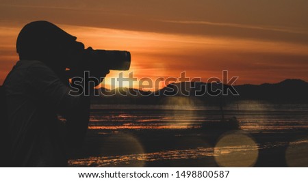 Traveler man take a photo by digital camera in sea side beach sunset so enjoying a beautiful nature.
