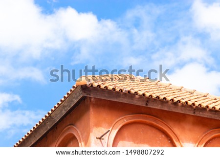 The roof of a vintage house has a backdrop of a bright blue sky.
