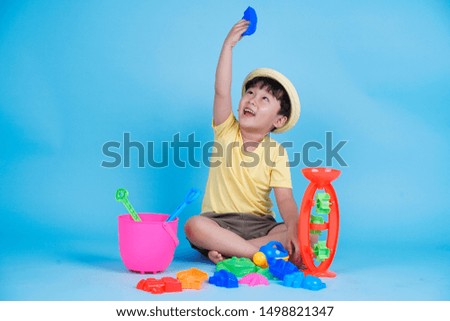 Asian little cute boy is playing with beach sand toys in studio, isolated on blue background with copy space