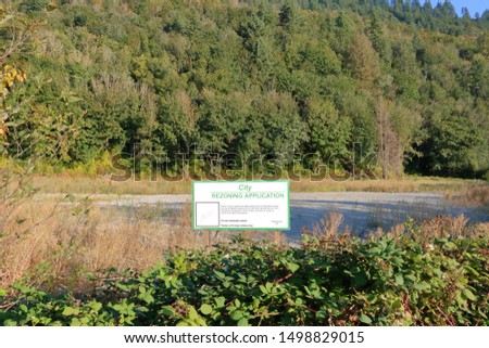Wide view of a large sign informing the public that there is an application to the city for rezoning the vacant land. 