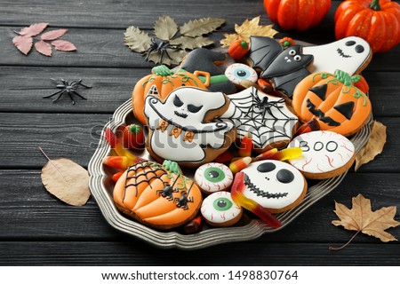 Halloween gingerbread cookies with candies and dry leafs on wooden table
