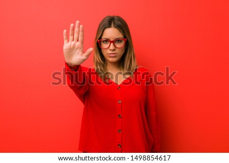 Young authentic charismatic real people woman against a wall standing with outstretched hand showing stop sign, preventing you.