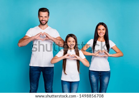 Portrait of charming family with brunette haircut making heart sign from their fingers wearing white t-shirt denim jeans isolated over blue background