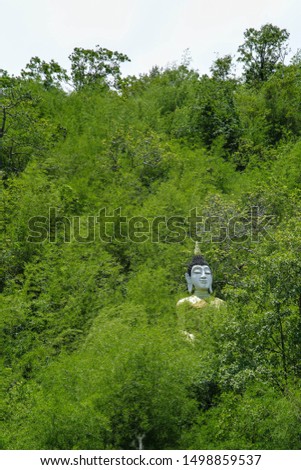 White stucco statue Is a sculpture of Thai people Built on a mountain that is like a forest Because there is a trees covered With natural green background And it is a sunny day. 