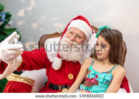 Santa Claus sitting with a girl on his lap making selfie photos with his cellphone.