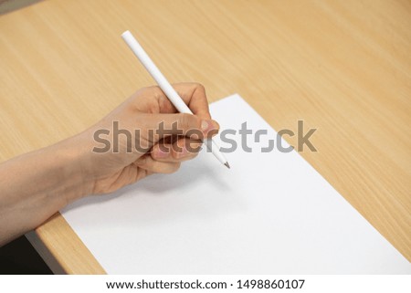 A closeup and detailed view on the hand and arm of a caucasian person holding a pen, writing on a blank sheet of white paper with copy-space on an office desk.