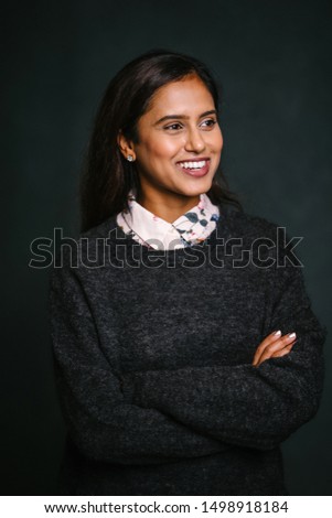 Studio portrait of a beautiful, attractive and young Indian Asian girl in a preppy outfit. She is wearing a white blouse and a dark sweater over it and is smiling happily for her profile head shot. 