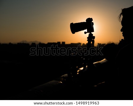 Silhouette of camera and asian photographer at Jingshan Park with Beijing skyline in background in sunset light, China