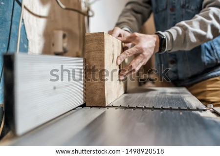 Caucasian man making wooden parts for custom furniture on machine tool called thickness planer in carpentry. Producing lumber concept Royalty-Free Stock Photo #1498920518