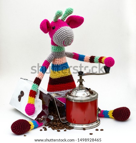Multi-colored Amigurumi giraffe grinds coffee with a manual coffee grinder.