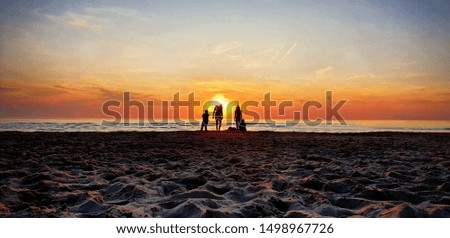 Silhouettes of people at a sandy beach enjoying the golden hour, watching the sunset.