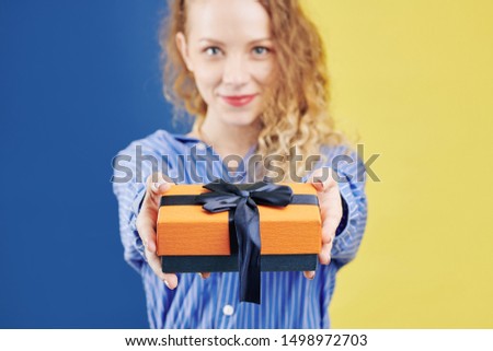Pretty smiling young woman giving you present with a big deep blue bow