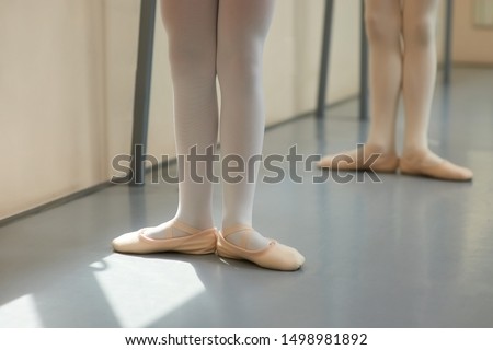 Legs of young ballerina in ballet pose. Little girl standing in pose at classical ballet studio, cropped image.