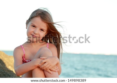 Charming young girl in a pink bathing suit sitting on a background of the sea/Girl on the Black Sea