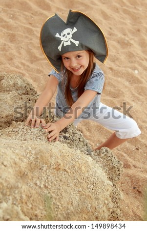 Adorable little girl in pirate hat looking for treasure on the beach on a sunny day