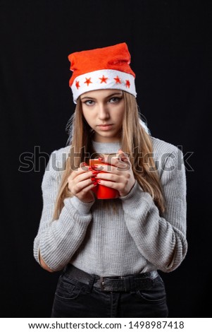 Beautiful girl with cup of tea posing on the black background in New Year outfit. Celebration.