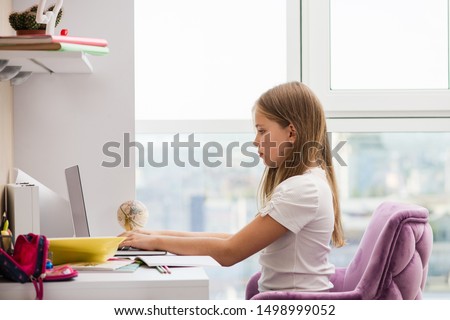 Beautiful school girl sit at desk in good posture. Large and bright window in background. Royalty-Free Stock Photo #1498999052