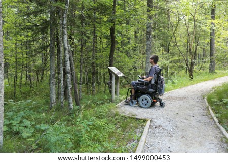Happy man on wheelchair in nature. Exploring forest wilderness on an accessible dirt path. Royalty-Free Stock Photo #1499000453