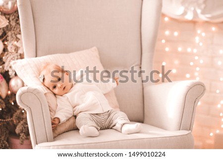 Cute baby sitting in chair over Christmas lights in room closeup. Looking at camera. Winter season holidays. Childhood. 