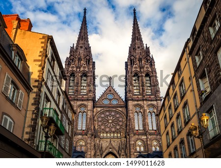 Beautiful, impressive cathedral of Clermont Ferrand in France, made dark from volcanic rocks lighten by golden sunset sun light and old, traditional French buildings Royalty-Free Stock Photo #1499011628