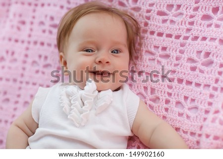 Sweet little baby girl lying on her back wearing a white jacket, looking at the camera and laughing  back.