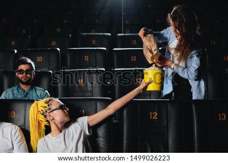 brunette girl giving popcorm to her friend with dreads before watching the film. close up photo. friendship, friends treating each other during the session
