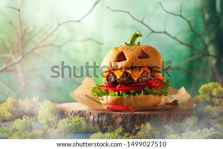 Halloween party burger in shape of scary pumpkin   on natural wooden board. Halloween food concept.