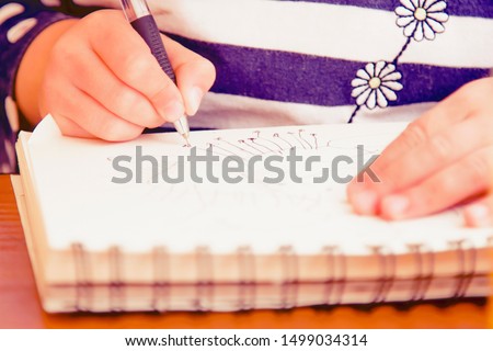 Humorous portrait of little female artist designer draws a pencil sketch  on notebook (creativity, art, training concept). Selective focus.