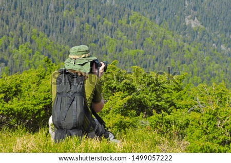 Photographer hiding in the bushes and taking pictures of nature. Photographer is taking a picture of landscape in mountains