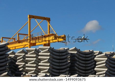 Large yellow crane and curved concrete precast segments for building a tunnel. A plane in the blue sky background. Precast concrete tunnel plant.