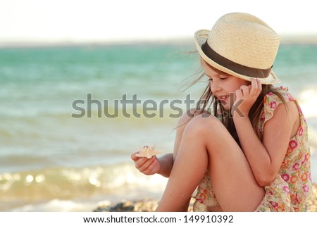 Caucasian cute young girl in a summer dress and hat holding a starfish on a beautiful background of the sea