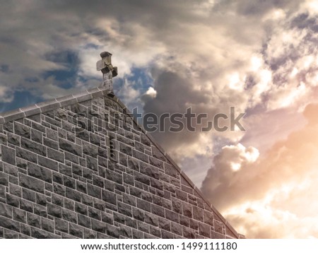 Catholic cross on top of a roof on dramatic sky background. Sun light haze.