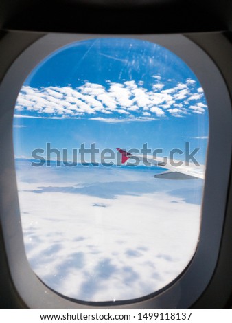 Picture taken from and through the window of an airplane, with bright colors, blue and clean sky with few clouds above