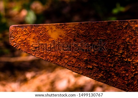 Closeup of rusted triangular metal flag pole in forest with blurred background.