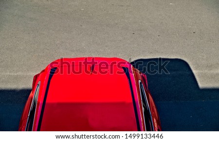 Red modern suv car parked in a black asplalt parking lot, top view of the rear section, sun and shade areas. 