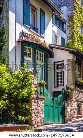 Downhill street with storey residential house with open wooden shutters and residential lofts and arched gates - a classic architectural design of old Paris on the hills of Montmartre with green ivy